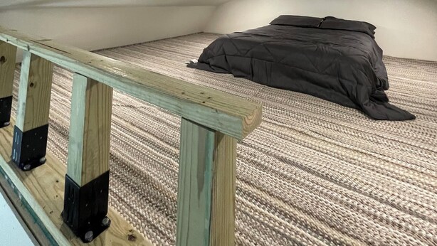 Un dormitorio bajo las tejas con techo inclinado, una cama individual y una barandilla de madera.