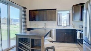 Una cocina moderna con una isla grande, armarios oscuros y vistas al exterior.