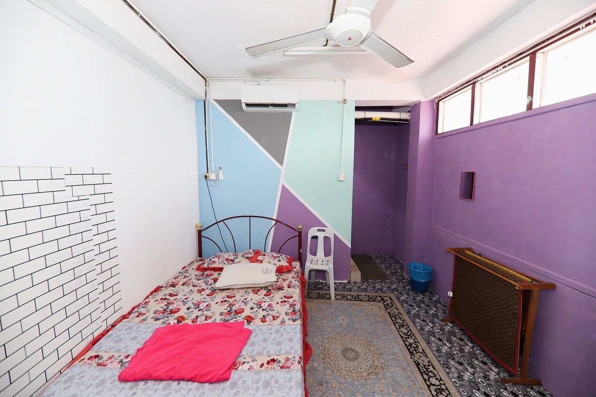 Een kleine, compacte kamer met een eenpersoonsbed, een plafondventilator, een airconditioning en een raam.