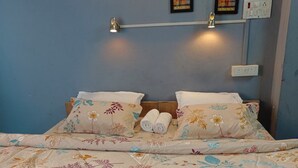 A bed with floral bedding, two wall-mounted lights, and three framed artworks on the wall. - Banaras Rest House  (Varanasi)
