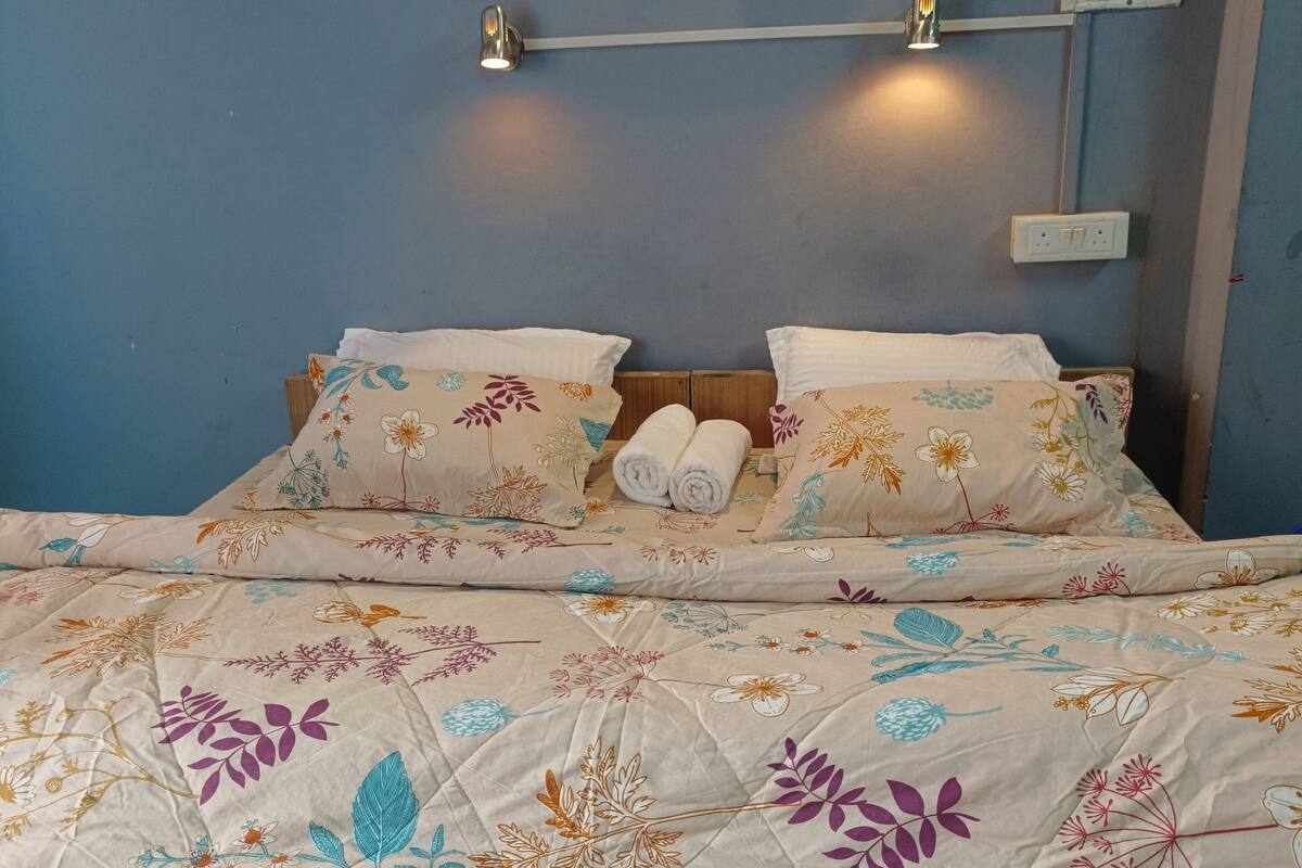 Un lit avec une literie à motifs floraux, deux lampes fixées au mur et trois œuvres d’art encadrées accrochées au mur.