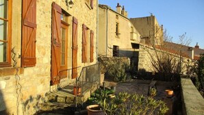 Un bâtiment en pierre avec des volets en bois, un escalier en pierre et des plantes en pot.