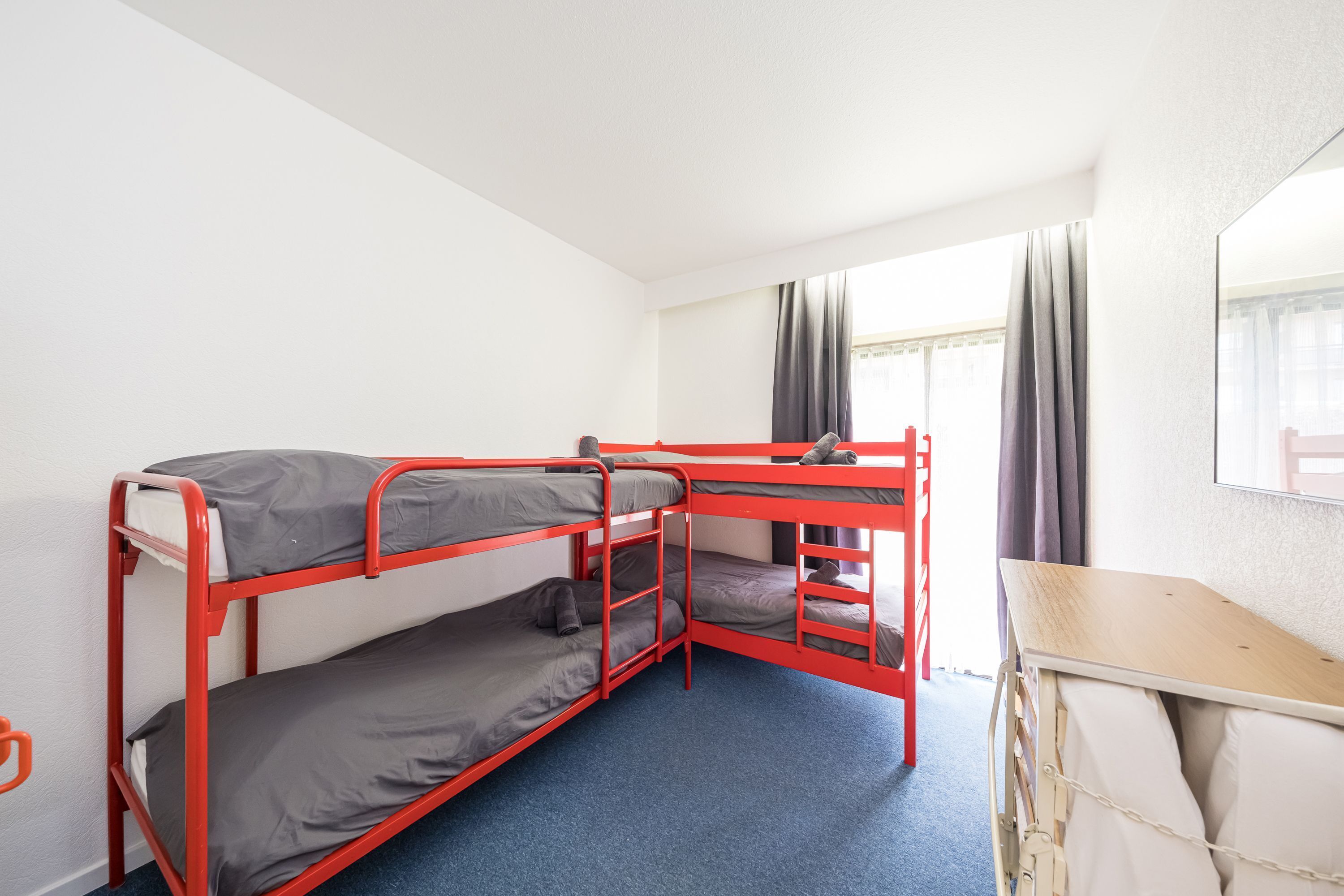 A bunk bed room with a desk and a window with curtains.