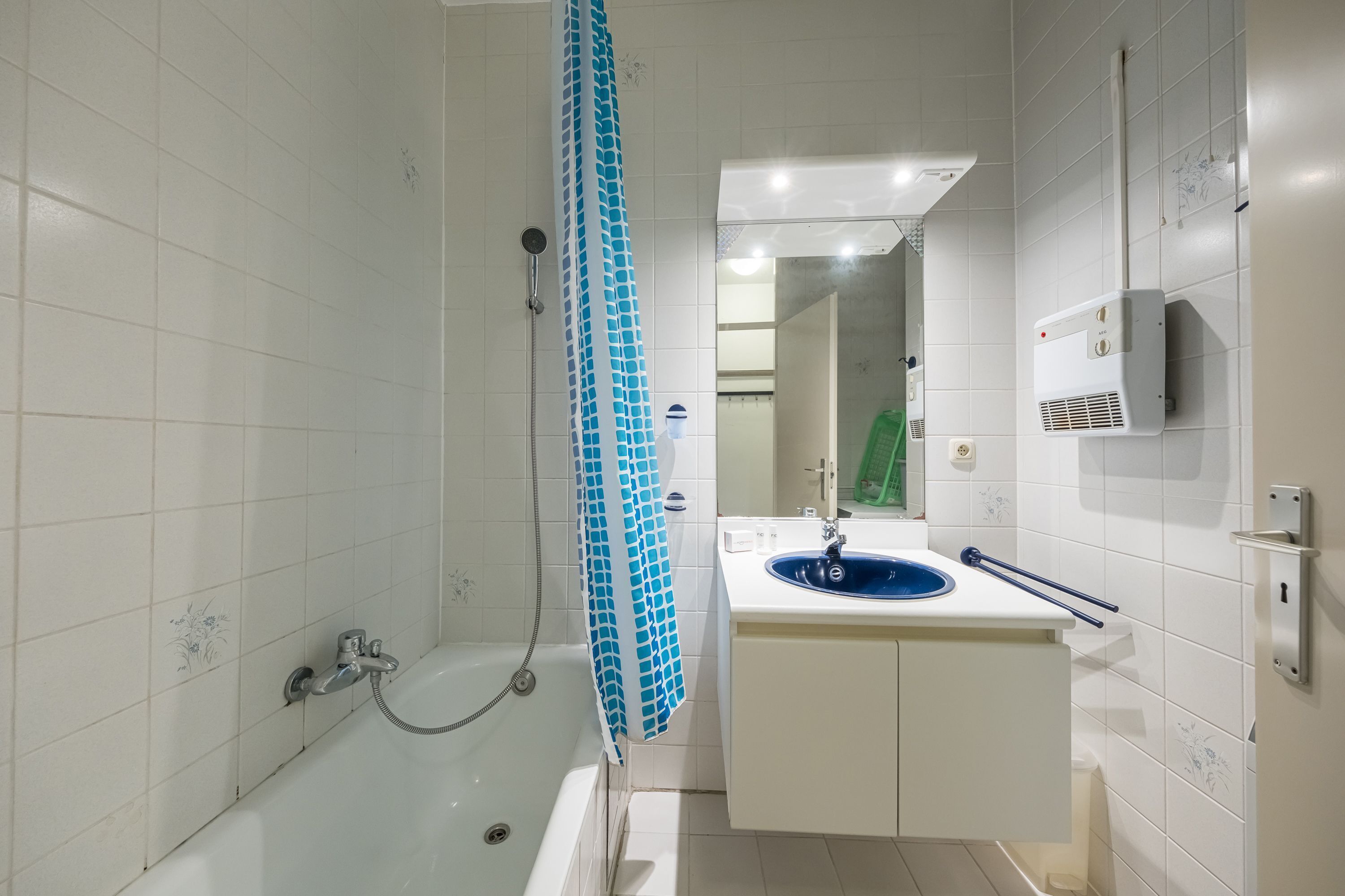 Une salle de bain avec une baignoire, un lavabo avec un receveur bleu et un porte-serviettes.