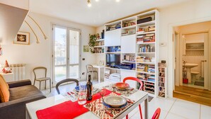 A modern living room with a dining area, a bookshelf, and a bathroom visible through an open door. - Appartamento Le Mimose In Lucca (Lucca)