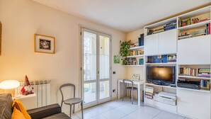 A modern living room with a sofa, a dining table, a TV, and a bookshelf. - Appartamento Le Mimose In Lucca (Lucca)