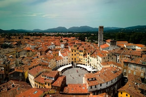 A historic town square surrounded by buildings with red-tiled roofs, a prominent tower, and a clear view of distant mountains. - Appartamento Le Mimose In Lucca (Lucca)
