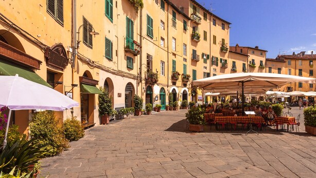 A courtyard with outdoor seating, stone paving, and yellow buildings with green shutters. - Appartamento Le Mimose In Lucca (Lucca)