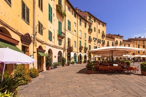 A courtyard with outdoor seating, stone paving, and yellow buildings with green shutters. - Appartamento Le Mimose In Lucca (Lucca)