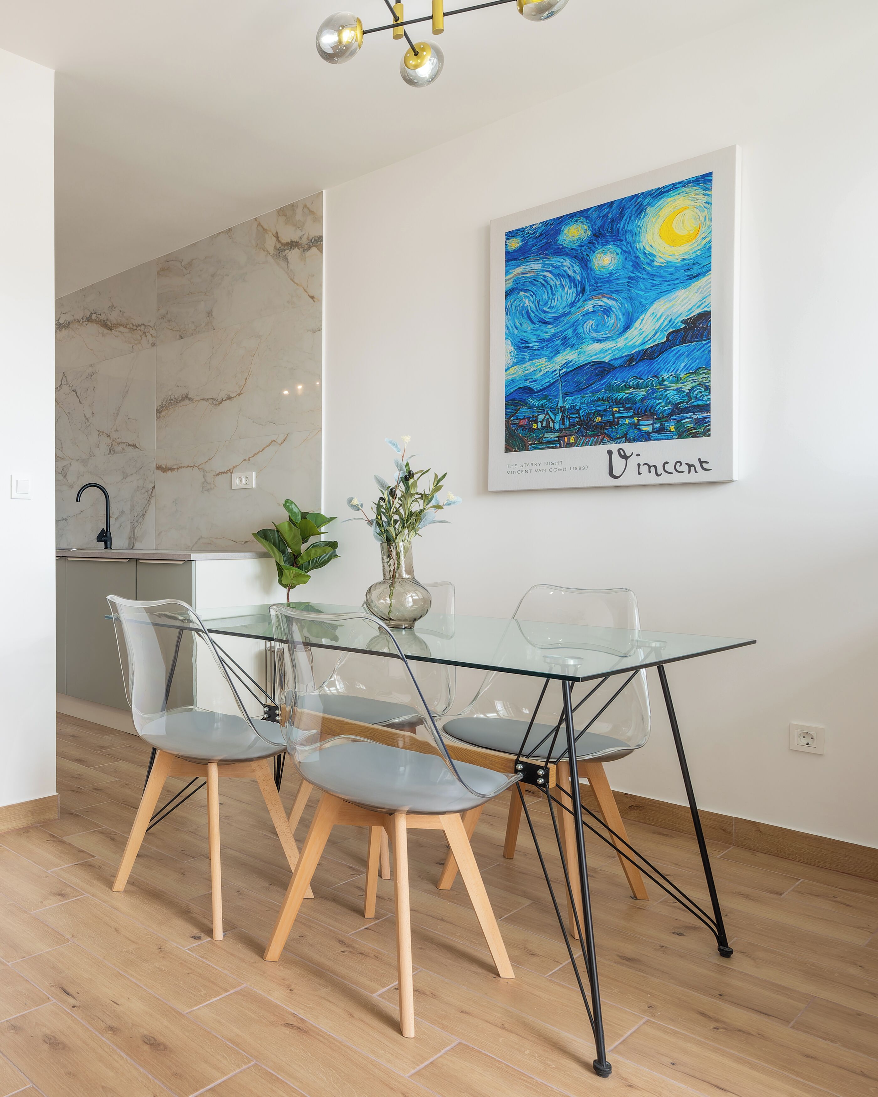 A dining area with a glass table, clear chairs, and a marble backsplash.