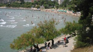Een strand met mensen die zwemmen en zonnebaden, omringd door gebouwen en bomen.