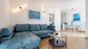 Een moderne woonkamer met een hoekbank, een glazen salontafel en kunstwerken aan de wanden.