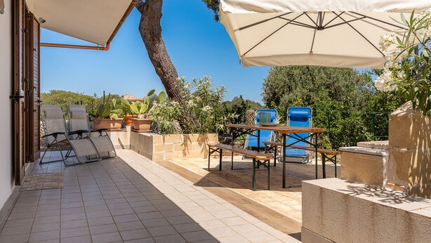An outdoor patio with tiled flooring, a table with benches, a large umbrella, and a blue trash bin. - Villetta al Plemmirio by Wonderful Italy (Syracuse)
