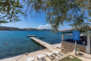 Un hotel frente al agua con zona de piscina, muelle y un cartel que indica habitaciones de hotel, apartamentos de lujo y un restaurante.