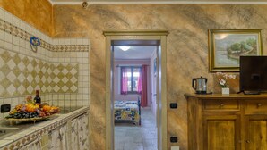A hotel room with a kitchen area, a bed with a colorful bedspread, a wooden cabinet, and a television. - Appartamento Uva Shared Pool (Roccastrada)