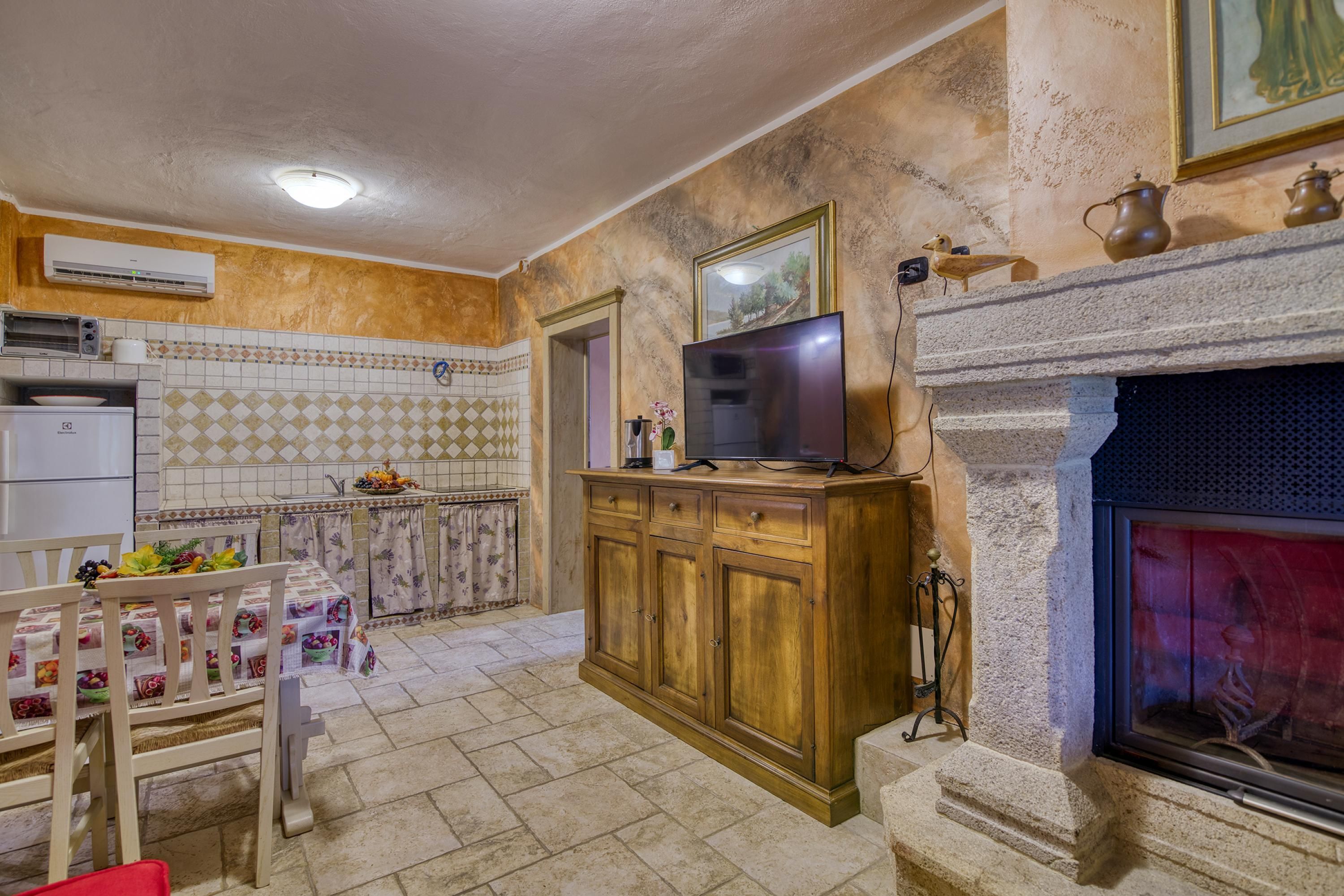 A kitchen with a tiled backsplash, a wooden cabinet, a television, and a fireplace.