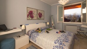 Un dormitorio con cama, escritorio, silla, ventana con vista y una obra de arte en la pared.