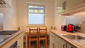 Una cocina compacta con mesa, sillas, tostadora, hervidor y pileta.