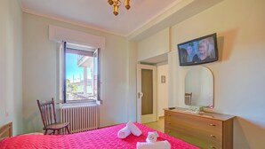 A hotel room with a bed, a wooden dresser, a television mounted on the wall, and a window with a view of the outside. - Il Giardino Di Dante Stresa Center (Stresa)