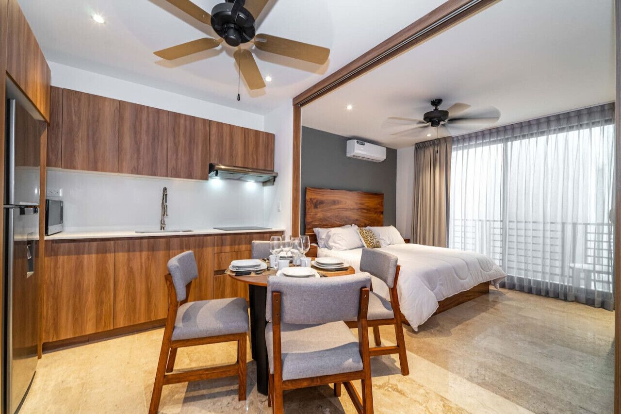 Een moderne hotelkamer met een eethoek, een bed met houten hoofdeinde en een groot raam met gordijnen.