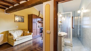 A living room with a wooden ceiling, a sofa, and a kitchen in the background. - Maramaldo Galestro Shared Pool Chianti (Castelfiorentino)