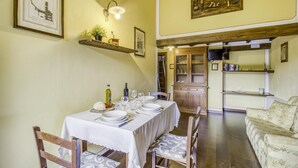 A dining area with a table set for four, wooden chairs, a chandelier, and a kitchen in the background. - Maramaldo Galestro Shared Pool Chianti (Castelfiorentino)