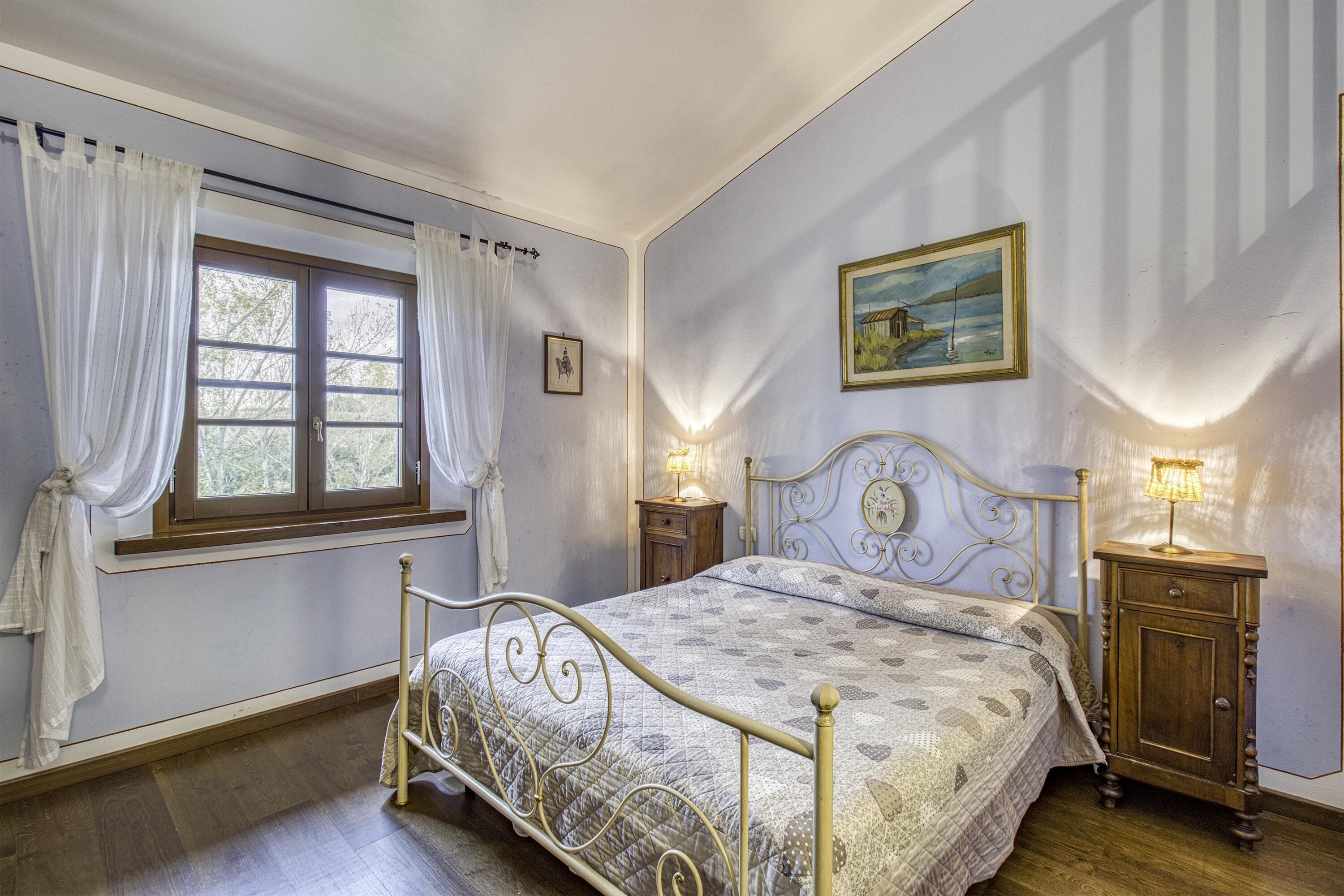 Une chambre à coucher avec un lit, une fenêtre avec des rideaux, une table de chevet avec une lampe et un tableau accroché au mur.