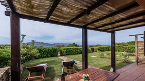 Une terrasse en bois avec une table et des chaises, donnant sur un jardin bien entretenu et offrant une vue magnifique sur la mer.