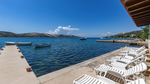 Une jetée avec des bateaux, une mer d’un bleu limpide et des chaises longues blanches.