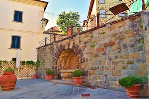 A stone archway leading to a courtyard with potted plants and a small fountain. - Casale Al Sole Tra Le Vecchie Vigne 6 (Radda in Chianti)