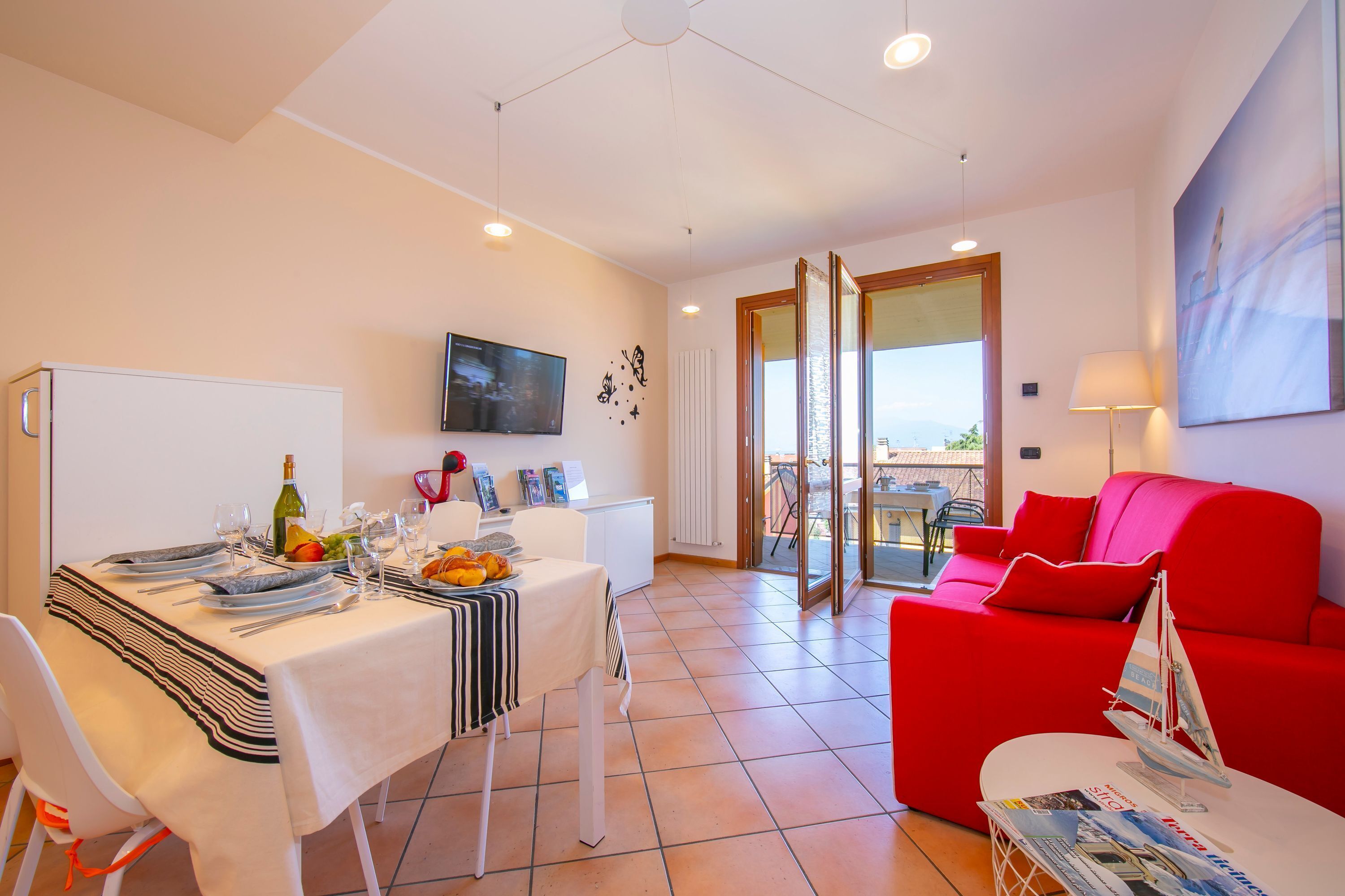 A dining area with a table set for four, a red sofa, and a balcony with a view.