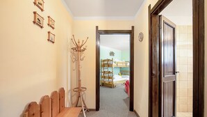 Um corredor com um banco de madeira, um cabideiro e uma porta que dá para um quarto com cama e cómoda.