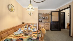 Uma sala de jantar com uma mesa comprida posta para refeição, cadeiras de madeira, um candelabro e um armário de madeira com louças.