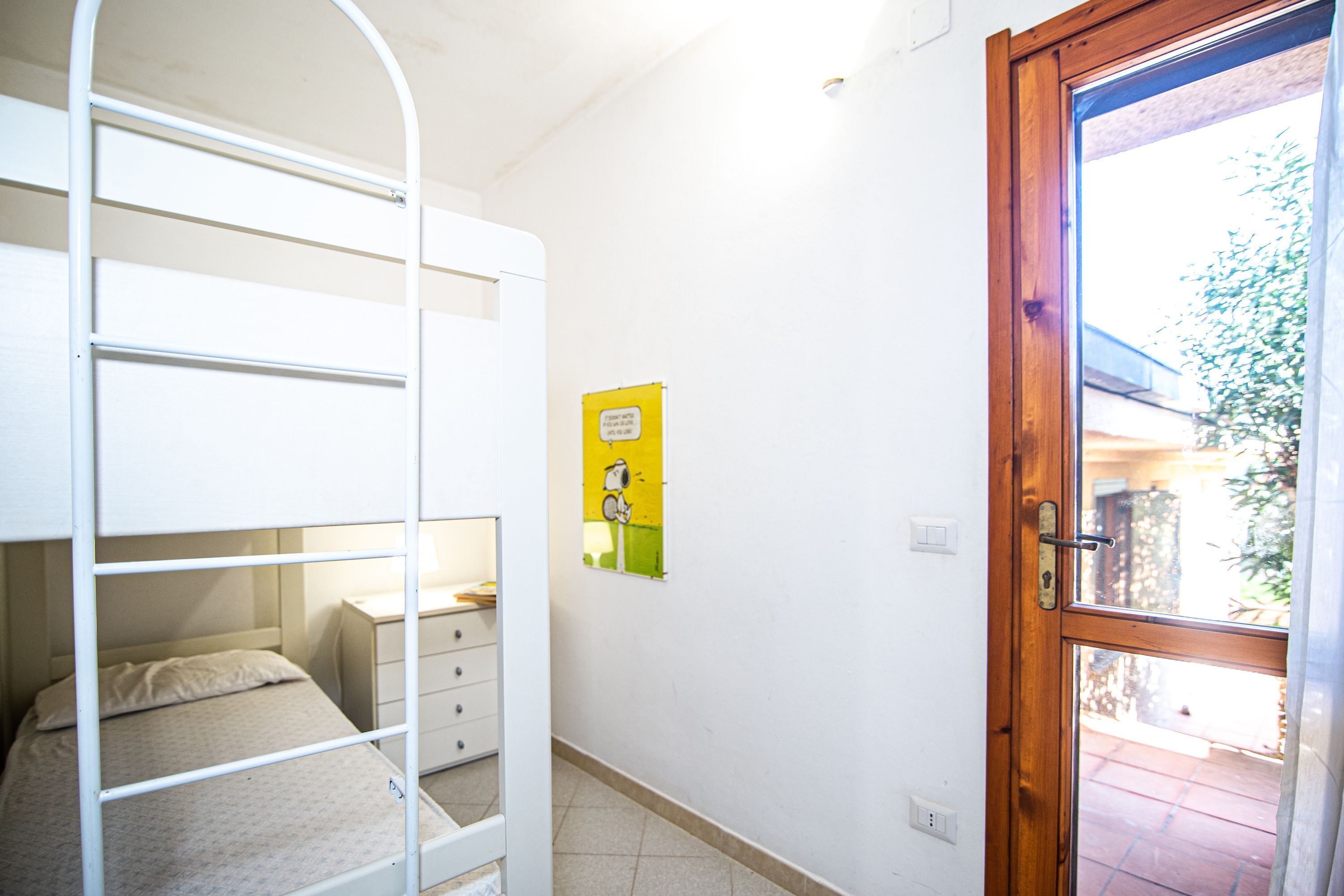 A dormitory room with bunk beds, a small desk, and a door leading outside.