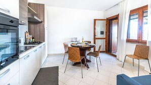Une cuisine compacte dotée d’appareils électroménagers modernes, un coin repas avec quatre chaises et une grande fenêtre laissant entrer la lumière naturelle.
