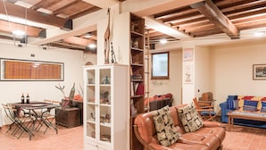 A spacious living area with a leather sofa, a dining table with chairs, a cabinet with glass doors, and a bookshelf. - Cornflower apt With Shared Pool (Castiglione del Lago)