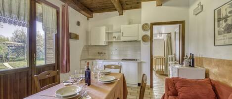 Un comedor con una mesa preparada para cuatro personas, sillas de madera, un sofá rojo y una cocina al fondo.