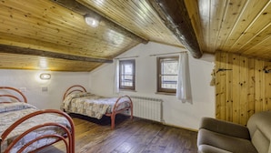 A room with wooden ceilings and walls, two beds with metal frames, a radiator, and a window. - Cornflower apt With Shared Pool (Castiglione del Lago)