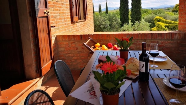 A patio with a table set for dining, a wine bottle, and a glass of red wine. There are potted plants and a view of the countryside. - Cornflower apt With Shared Pool (Castiglione del Lago)