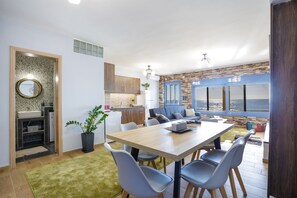A modern kitchen with a stone backsplash, a dining area with a large table and chairs, and a view of the ocean through large windows. - Maritinas Stone Apartment On The Beach (Pyrgos)