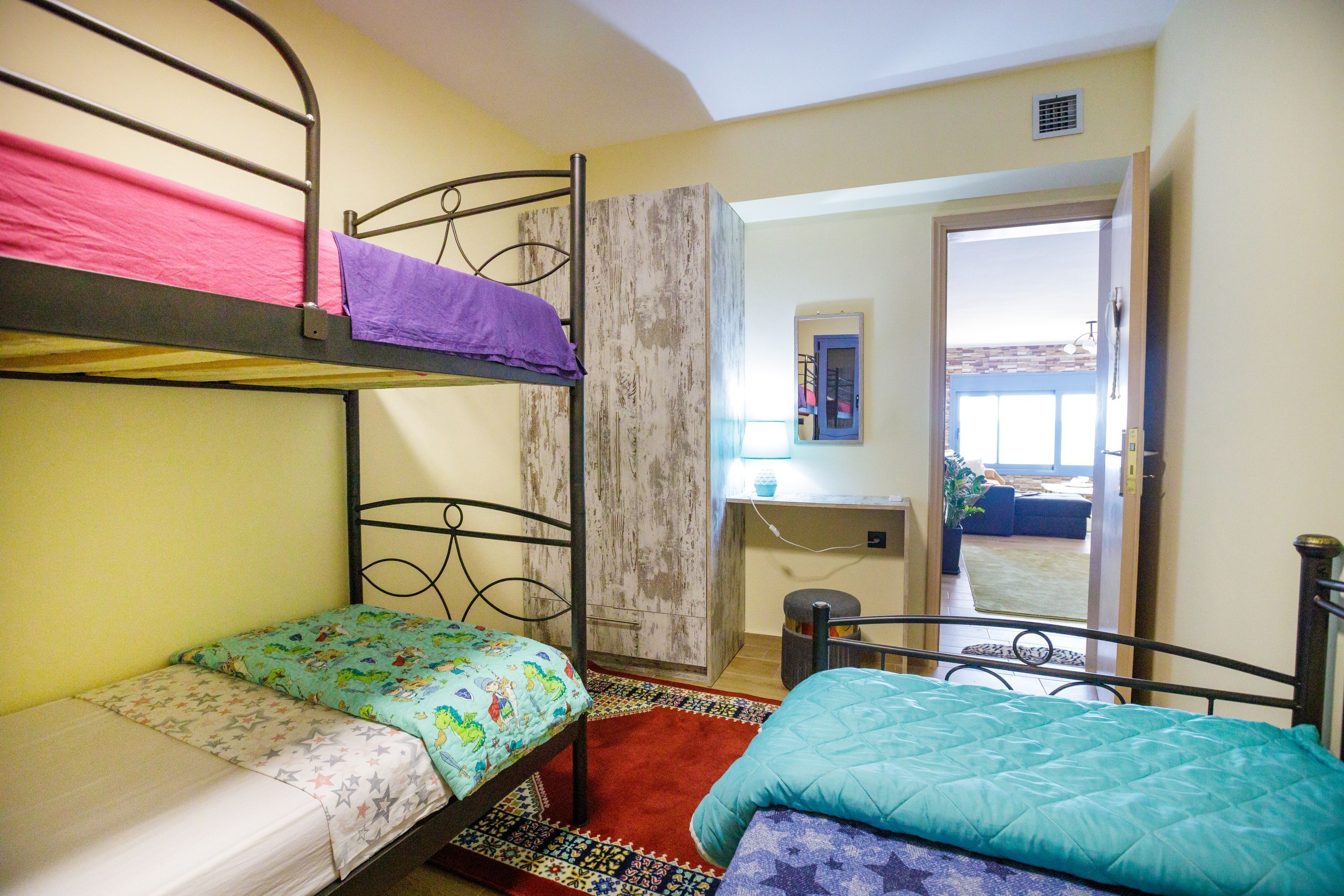 A dormitory room with bunk beds, a desk, and a view of the outside.