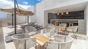 Eine Terrasse im Freien mit Liegestühlen, einem Holztisch und einer Barbereich mit einer Wand aus Stein.