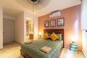 Un dormitorio con cama, lámpara de noche, aire acondicionado de pared y cuadros en la pared.