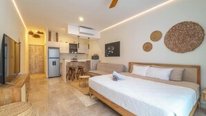 A modern hotel room with a large bed, a kitchenette, a ceiling fan, and a TV. - Stylish Boho Studio + Rooftop Pool @ Aldea Zama (Tulum)