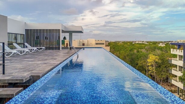 A rooftop infinity pool with a clear view of the city skyline, modern architecture, and a seating area with lounge chairs. - Stylish Boho Studio + Rooftop Pool @ Aldea Zama (Tulum)