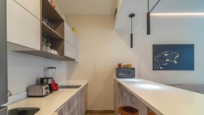A modern kitchen with a white countertop, a toaster, a blender, and a microwave. There is a wooden stool and a bar stool under the counter. - Stylish Boho Studio + Rooftop Pool @ Aldea Zama (Tulum)