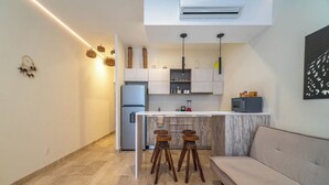A modern kitchen with a central island, bar stools, and a sofa in a living area. - Stylish Boho Studio + Rooftop Pool @ Aldea Zama (Tulum)