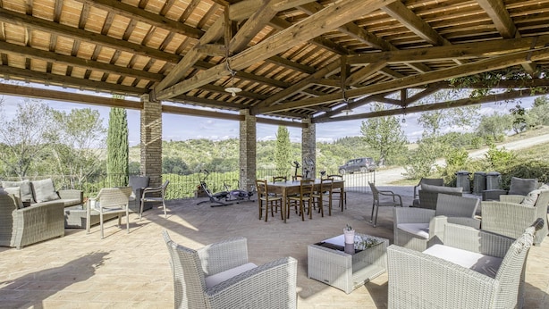 An outdoor patio with wicker furniture, a dining table, and a stone floor. - Maramaldo Sangiovese Shared Pool Chianti (Castelfiorentino)