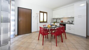 A modern kitchen with white cabinets, a dining table with red chairs, and a window with curtains. - Le Betulle Garden in Laveno (Laveno Mombello)