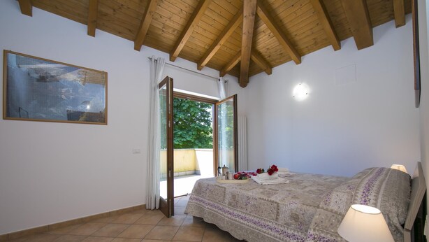 A bedroom with a bed, a nightstand, a lamp, a painting, and a window with curtains. - Le Betulle Garden in Laveno (Laveno Mombello)